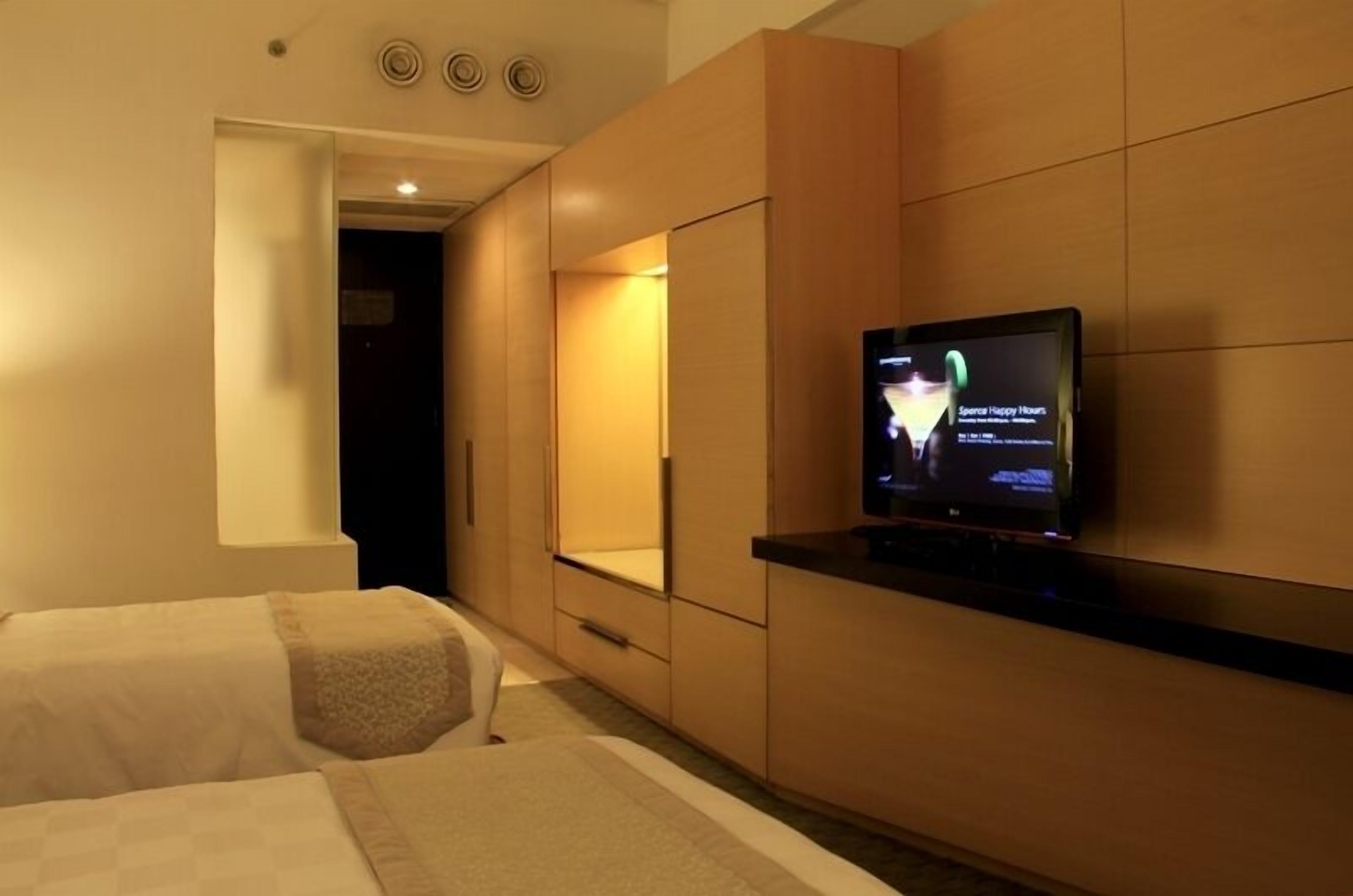 A hotel room with two beds, a TV mounted on the wall, and a large mirror.