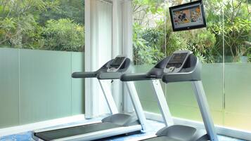 A room with two treadmills, a blue patterned carpet, and a large window with a view of greenery.
