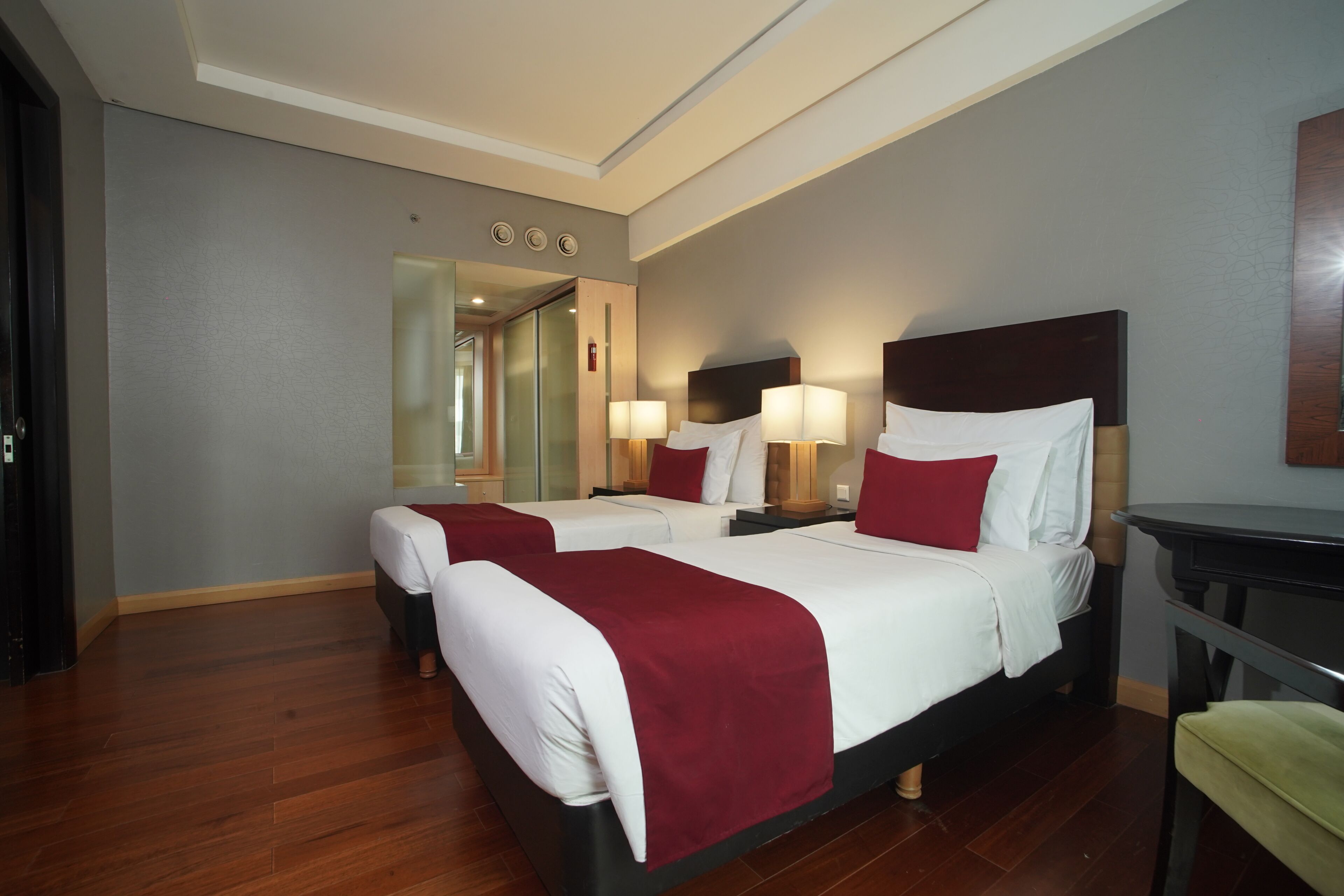 A hotel room with two beds, a mirror, bedside lamps, a nightstand, and a wooden floor.