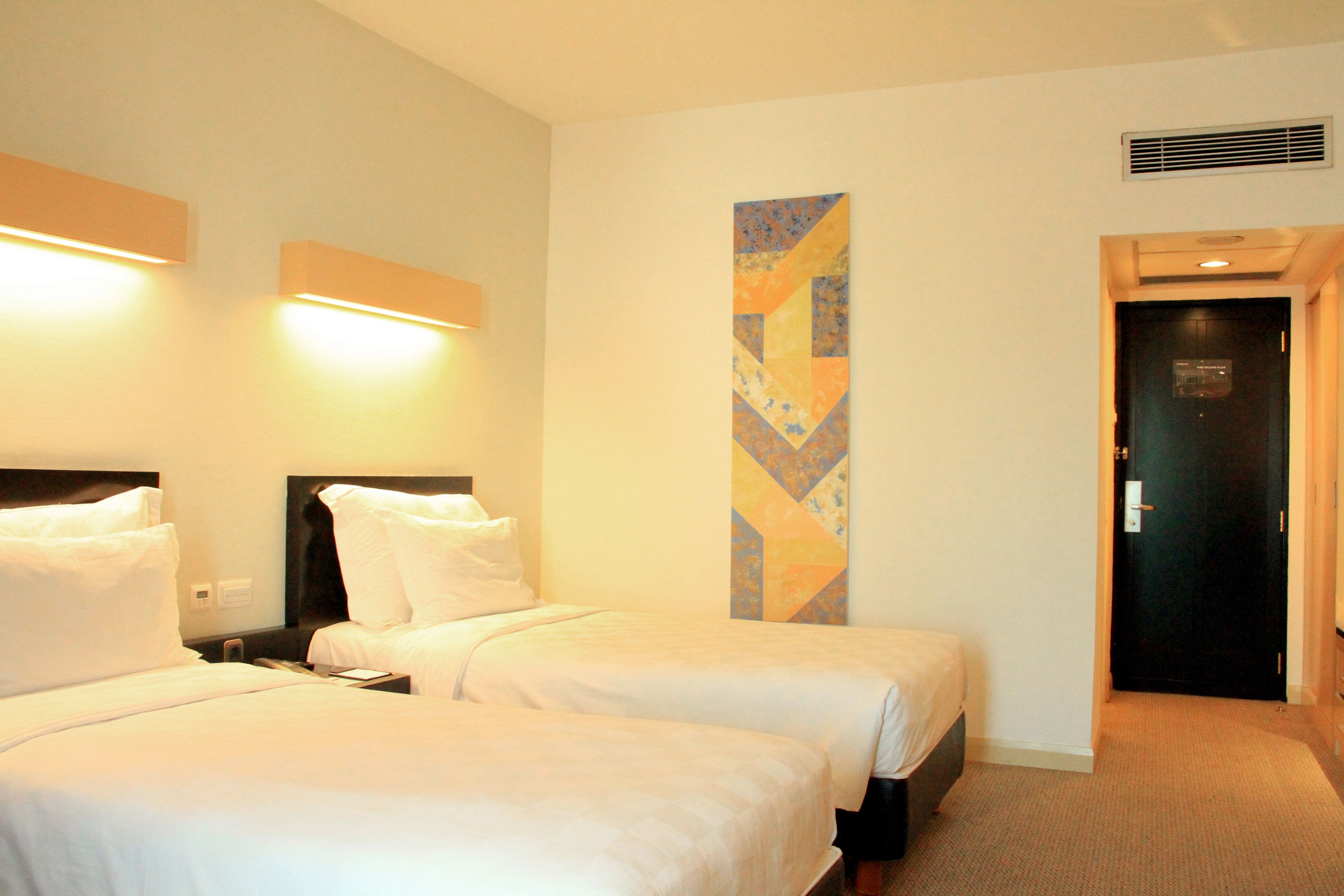 A hotel room with two beds, a nightstand, a wall-mounted artwork, and a door.