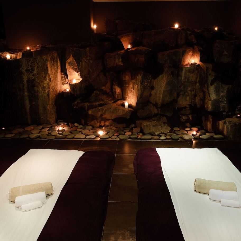 A spa room with two massage tables, a stone wall with candles, and a small rock garden.