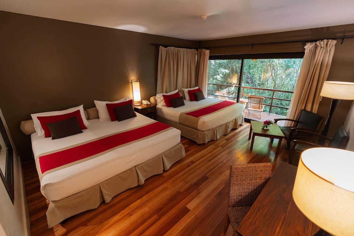 A hotel room with two beds, a balcony, a desk, and a chair.