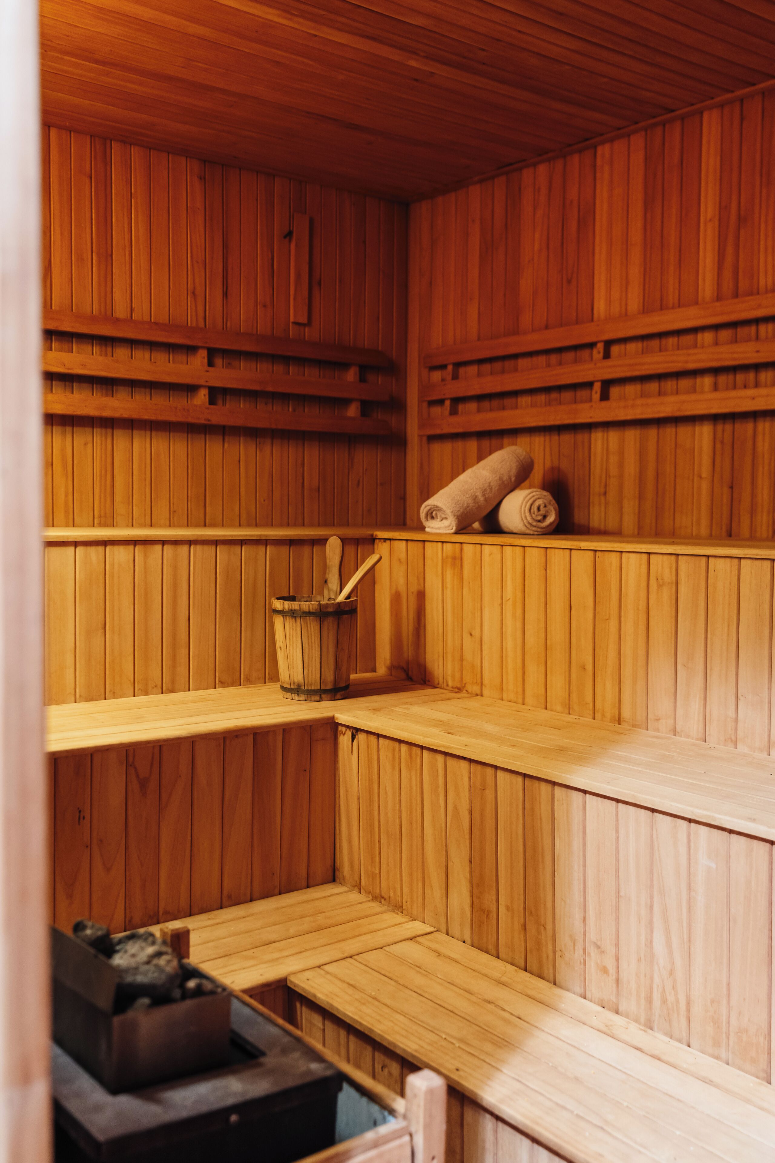 A wooden sauna with benches, a wooden bucket, and towels.