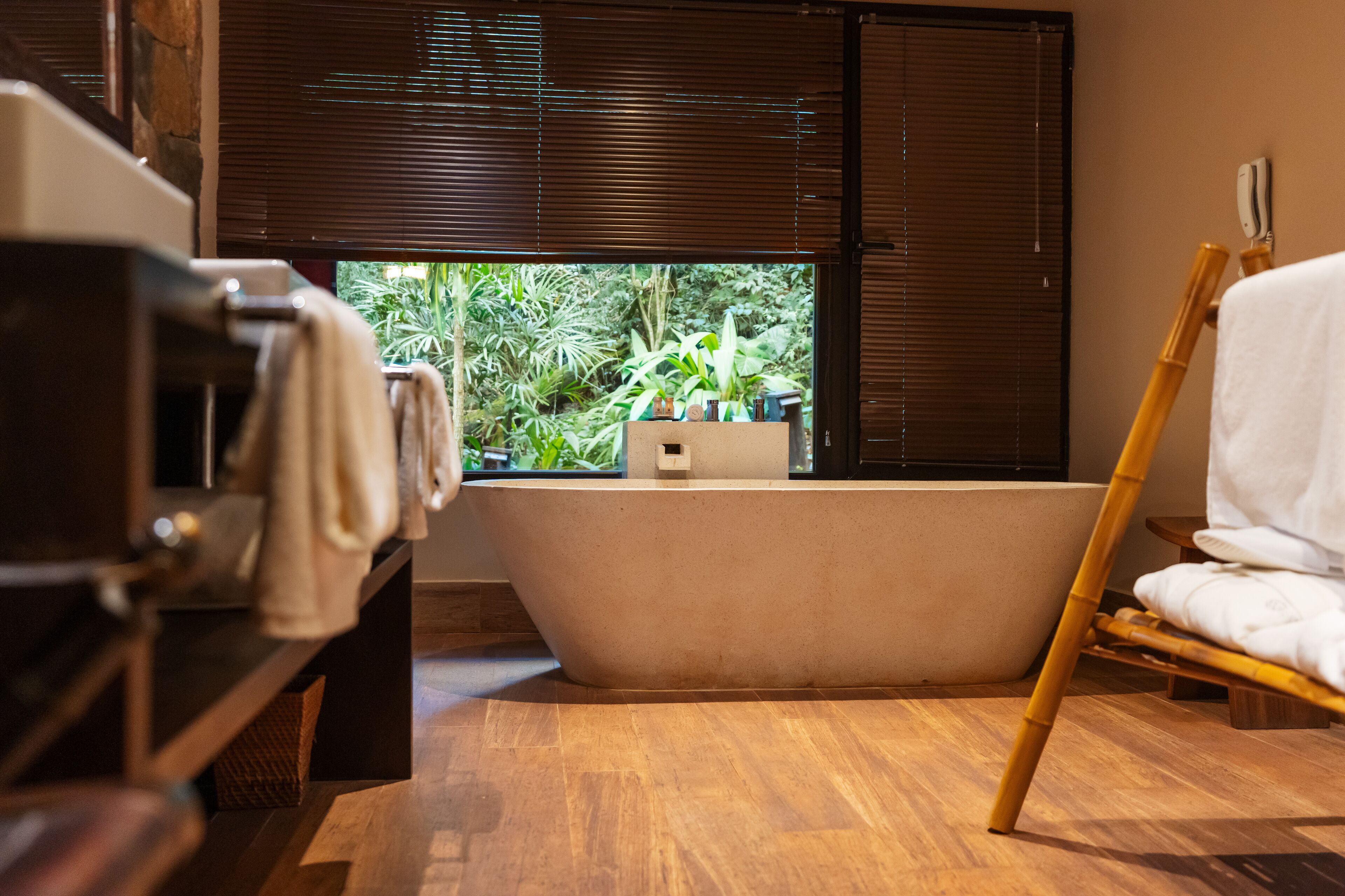 Un baño con bañera, suelo de madera y ventana con persianas.