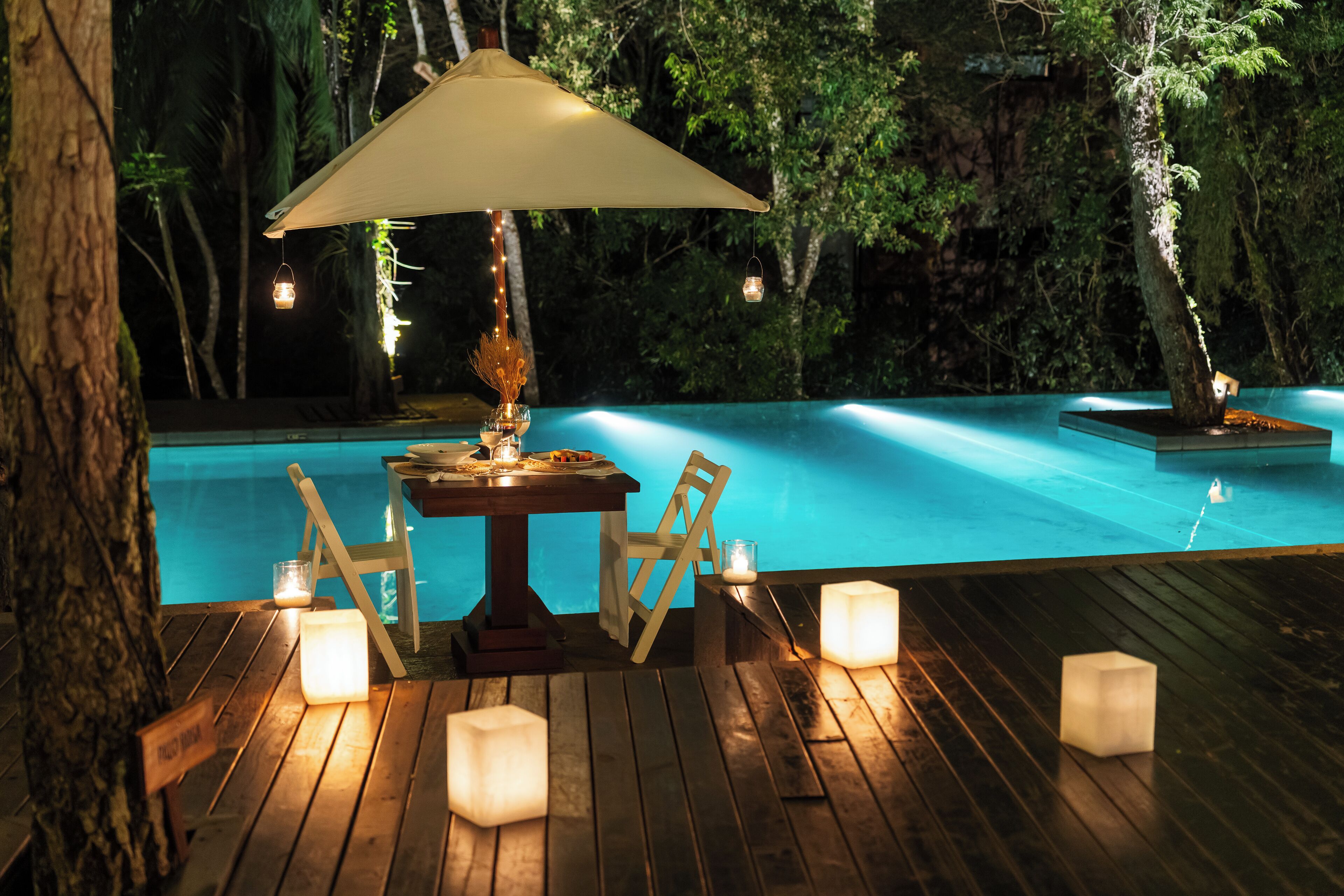 Ein Außenpoolbereich mit Holzterrasse, einem Tisch mit Stühlen und einem großen Sonnenschirm, der Schatten spendet.