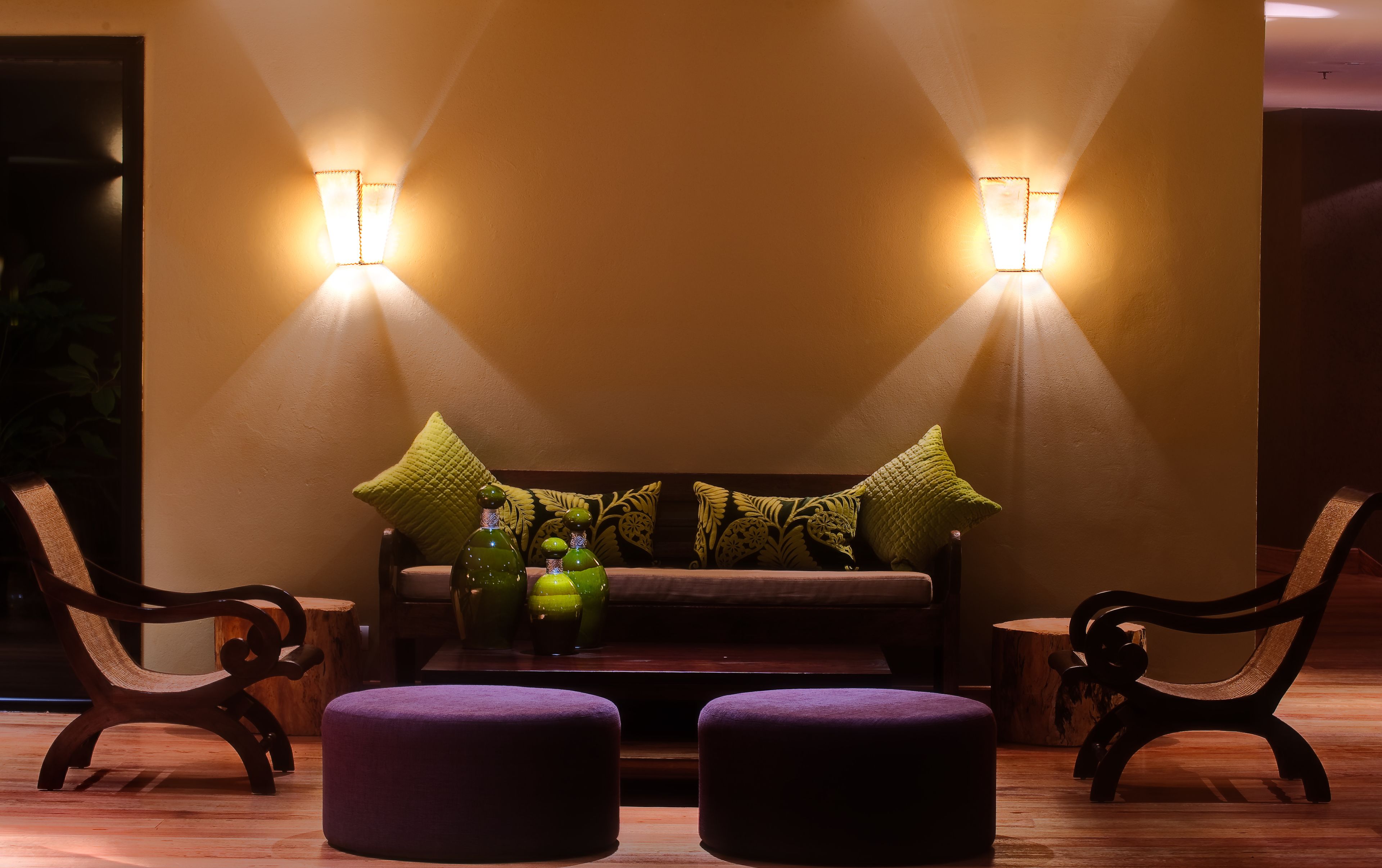 A seating area with a sofa and two chairs, a small table with decorative bottles, and two wall-mounted lights.