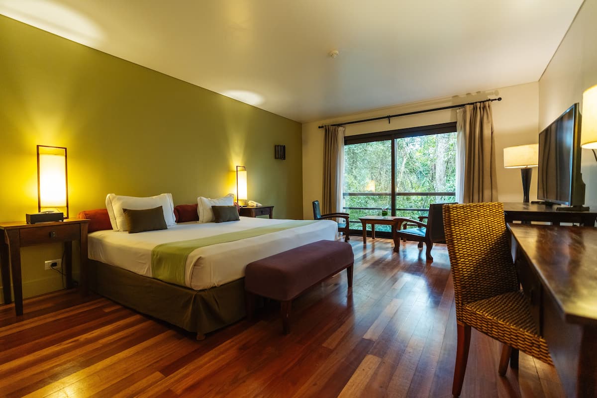 A hotel room with a large bed, a desk, a chair, and a window with curtains.