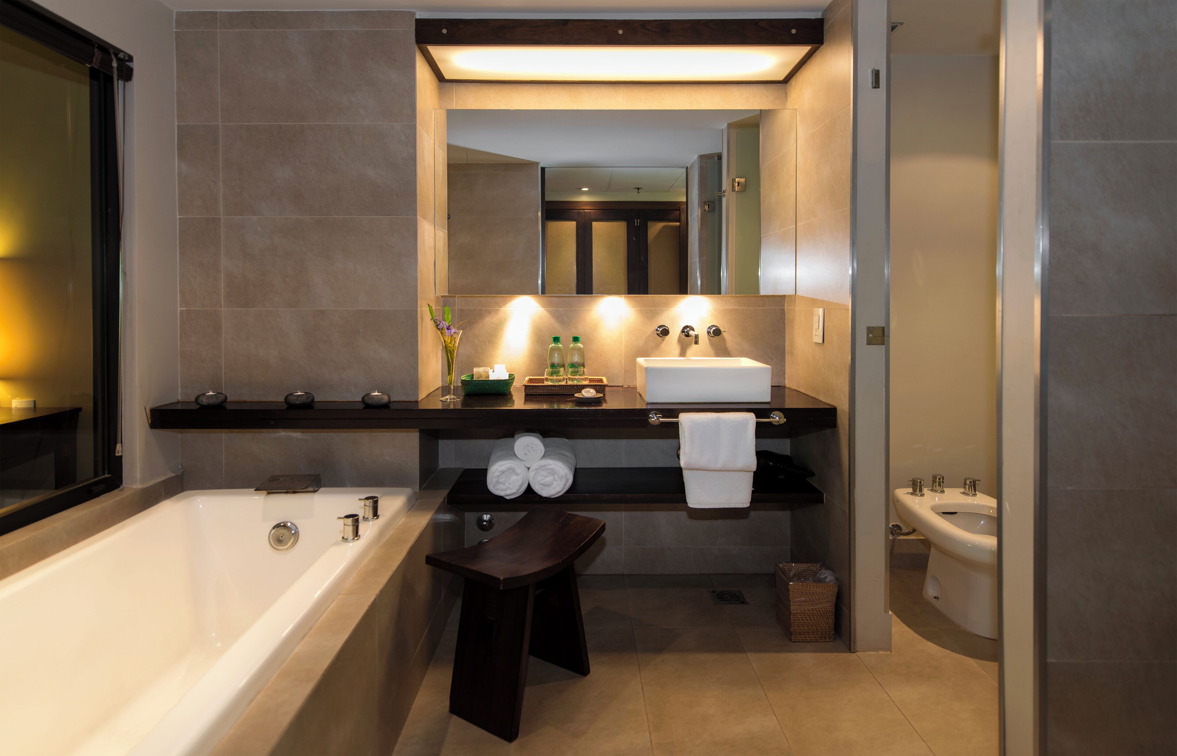 A modern bathroom with a bathtub, a sink, a bidet, and a vanity with a mirror.