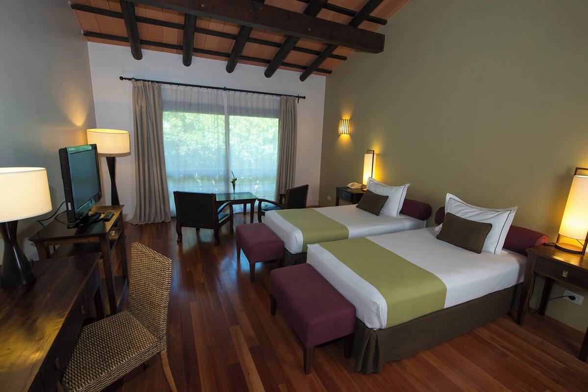 A hotel room with two beds, a desk with a computer, a chair, and a table with a lamp.