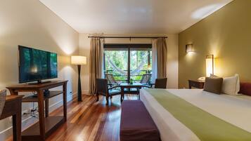 A hotel room with a bed, a desk with a television, a table with chairs, and a window with curtains.