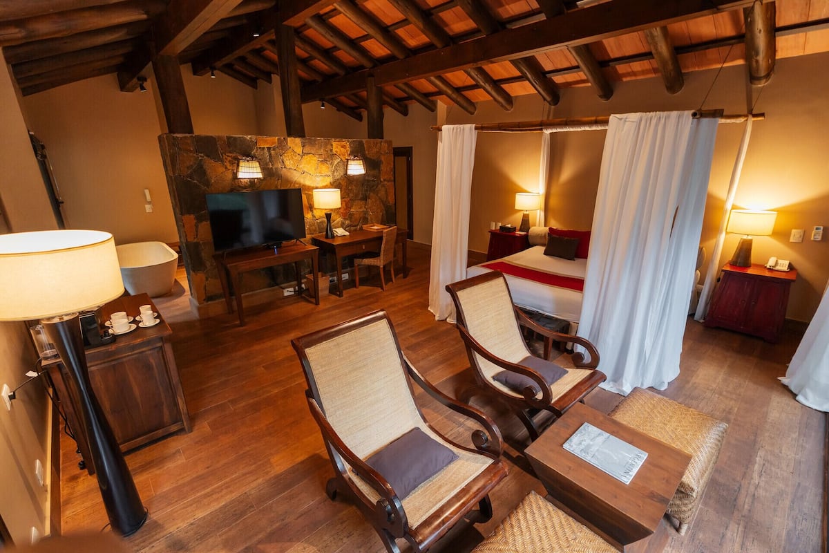 A cozy room with a stone fireplace, a television, a bed with white curtains, and wooden furniture.