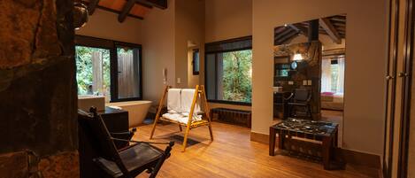 Una habitación amplia con piso de madera, una silla colgante, una mesa y vistas al exterior a través de amplias ventanas.