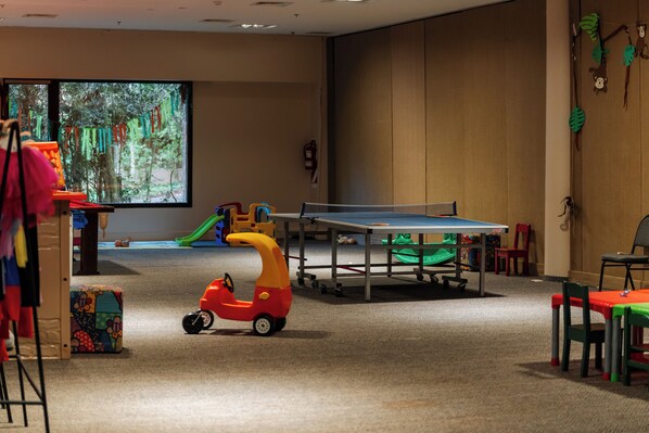 A playroom with a ping pong table, colorful toys, and a projector screen displaying a forest scene.