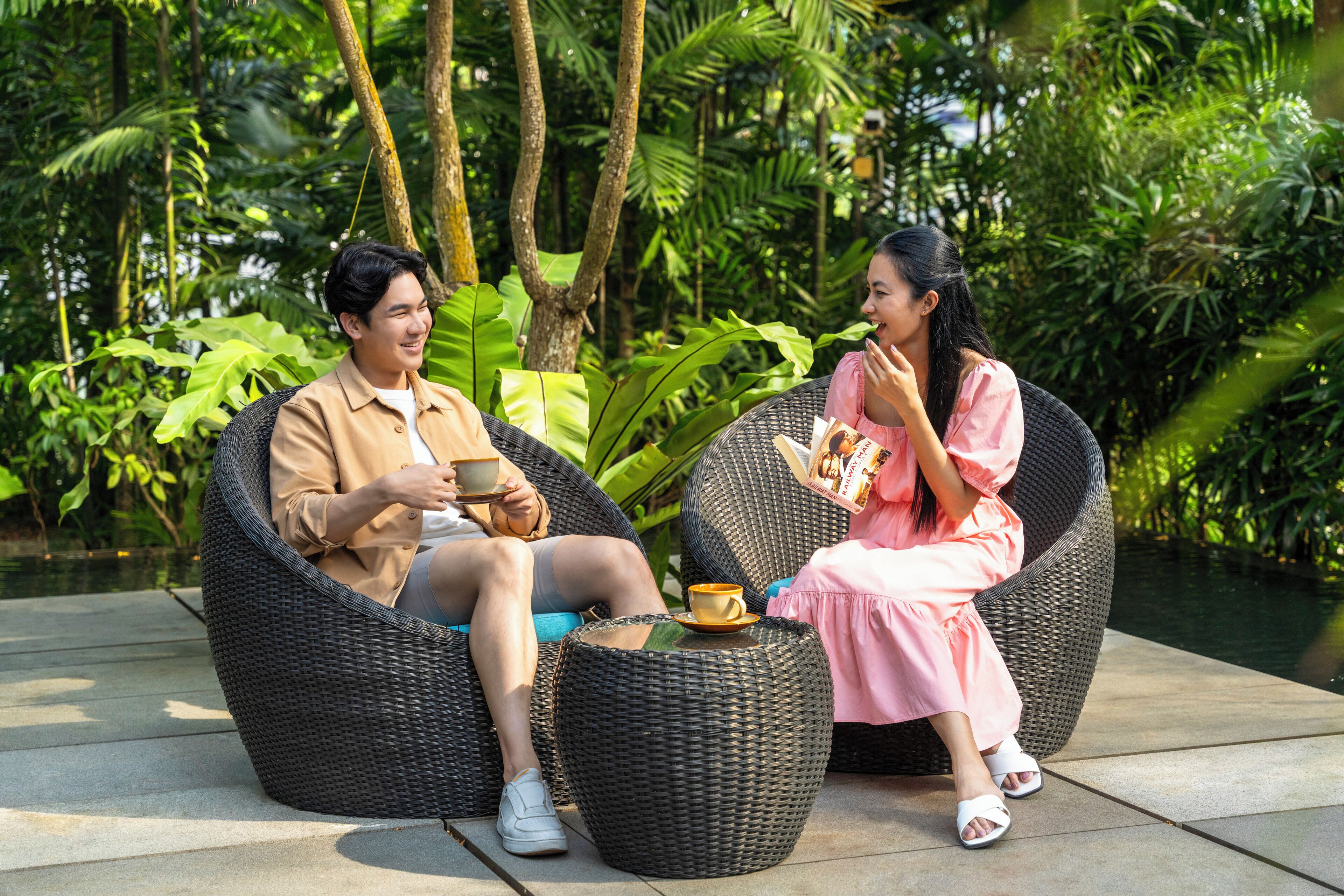 Two people sitting on wicker chairs outdoors with a table between them.