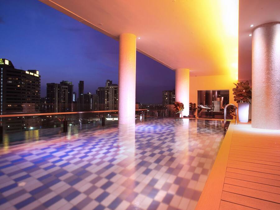 A modern hotel lobby with a checkered floor, large columns, and a view of the city skyline at dusk.