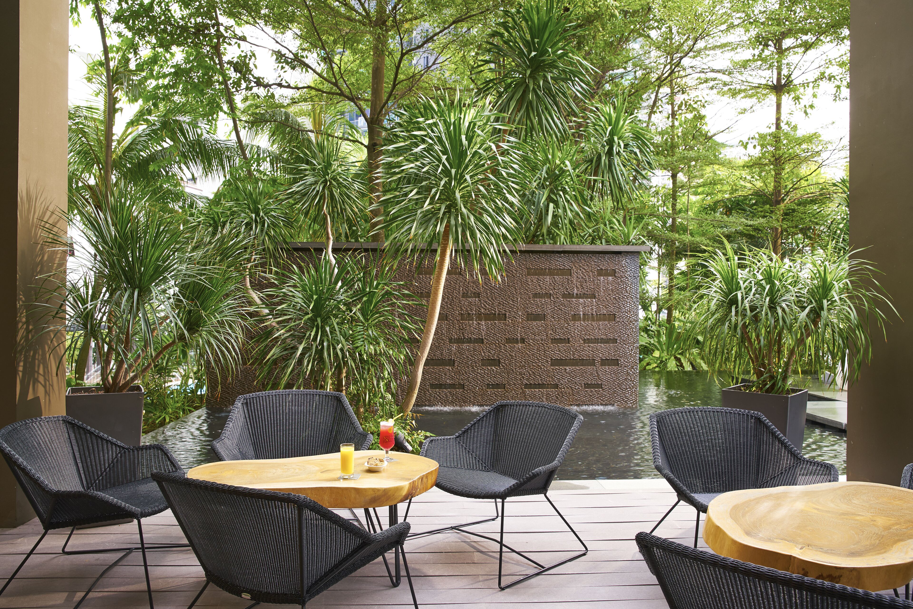 An outdoor patio with wicker furniture, a wooden table, and a small pond.