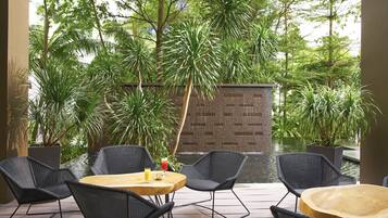 An outdoor patio with wicker furniture, a wooden table, and a small pond.