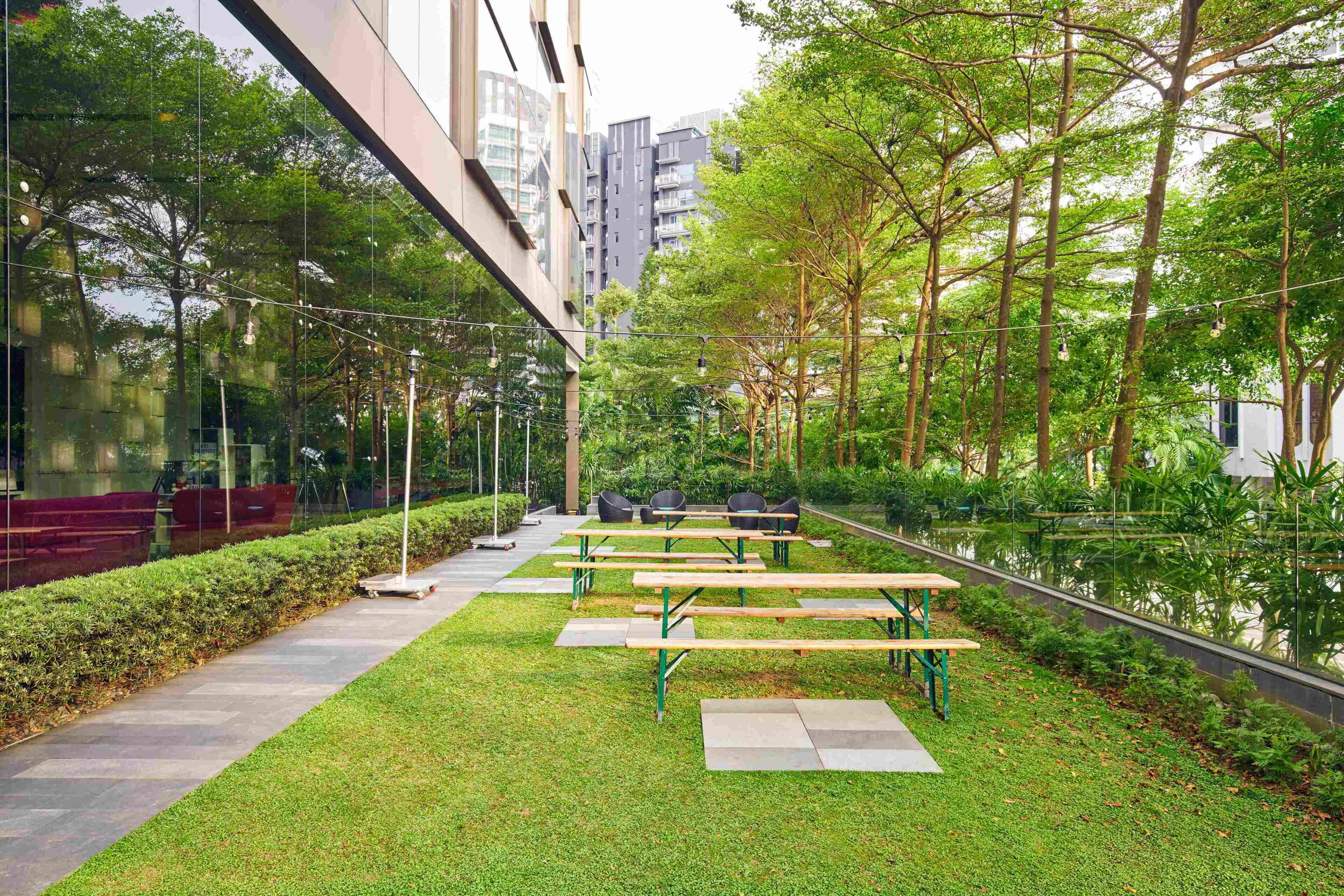 Un espace extérieur aménagé avec des tables et des chaises, entouré de verdure et agrémenté d’un élément décoratif aquatique dont la surface réfléchit la lumière.