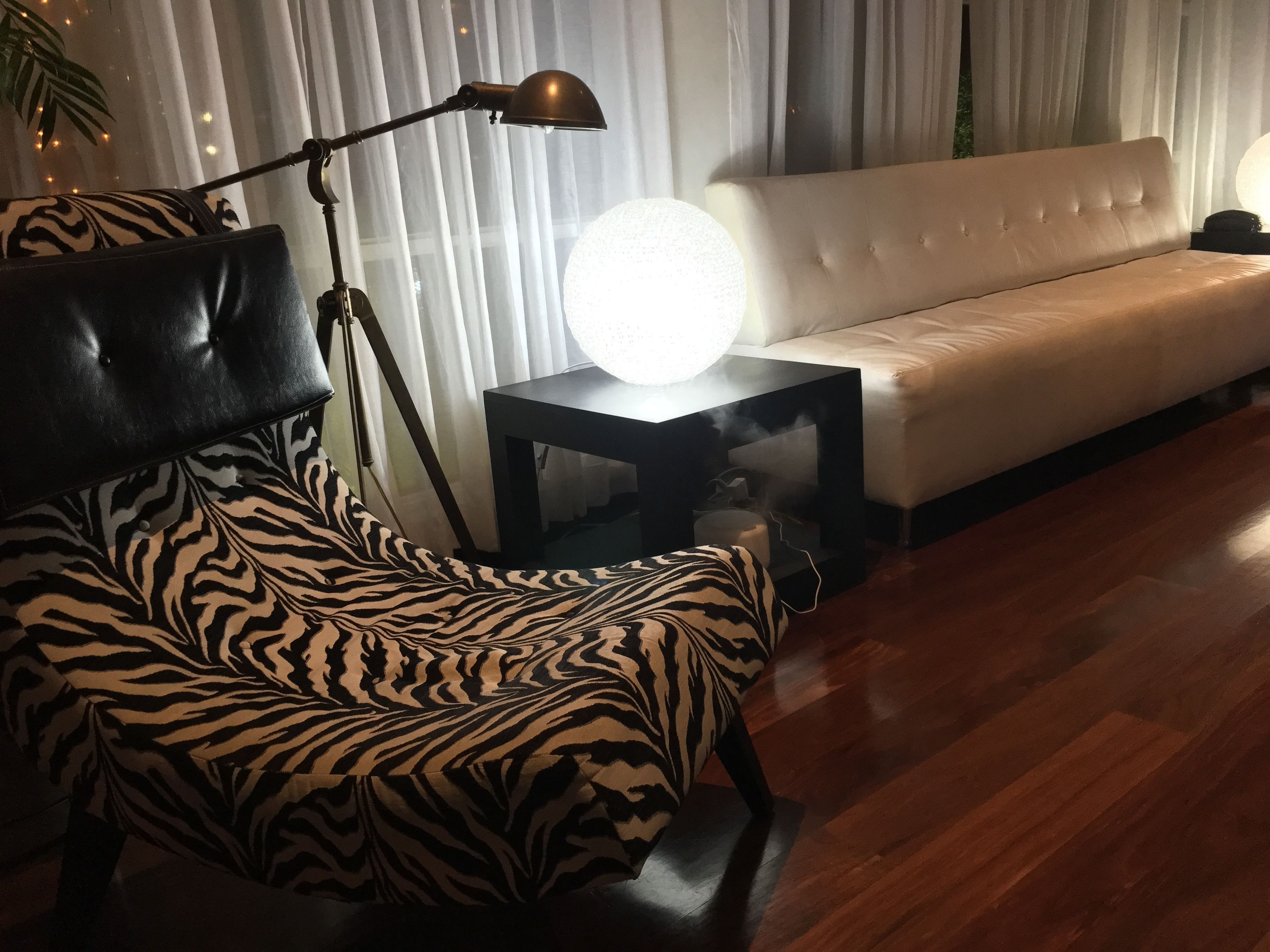 Ein modernes Wohnzimmer mit einem Stuhl in ZEBRA-Muster, einem schwarzen Beistelltisch mit einer kugelförmigen Lampe und einem weißen Sofa.