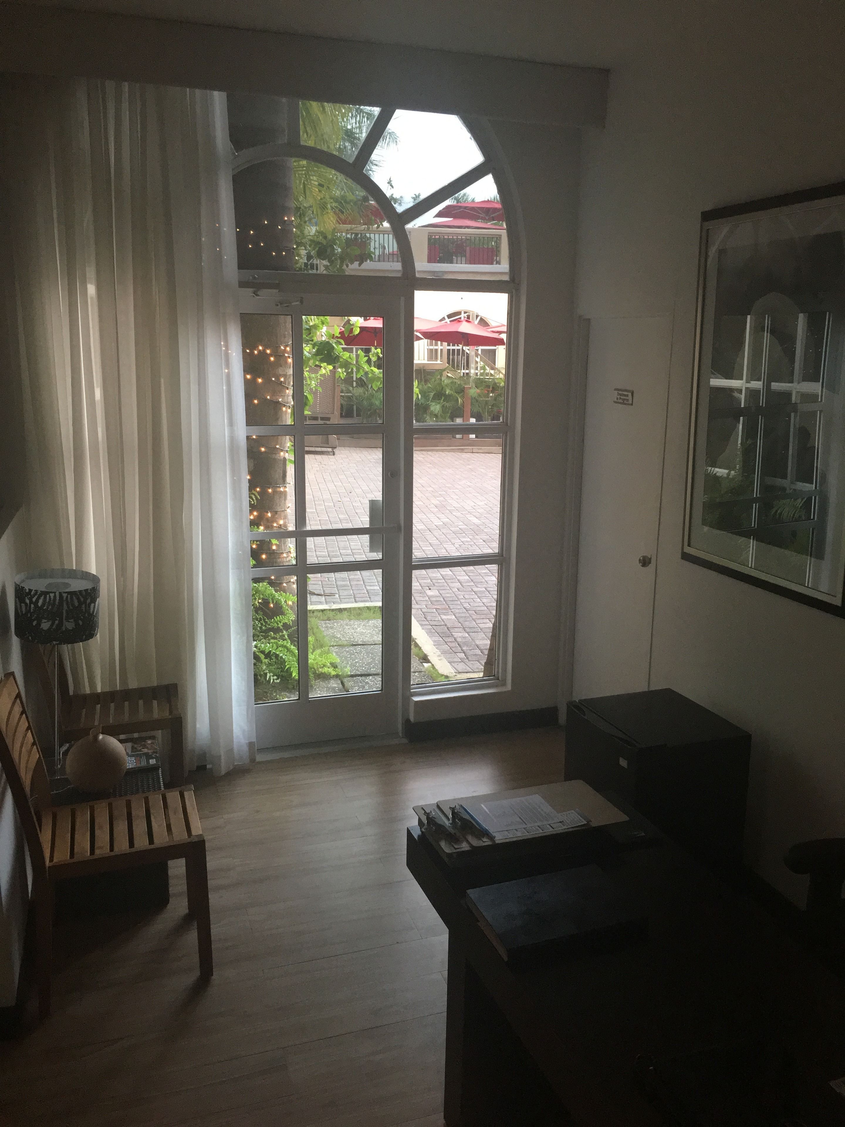 A room with a wooden bench, a table, and a large window with a view of an outdoor area with umbrellas.