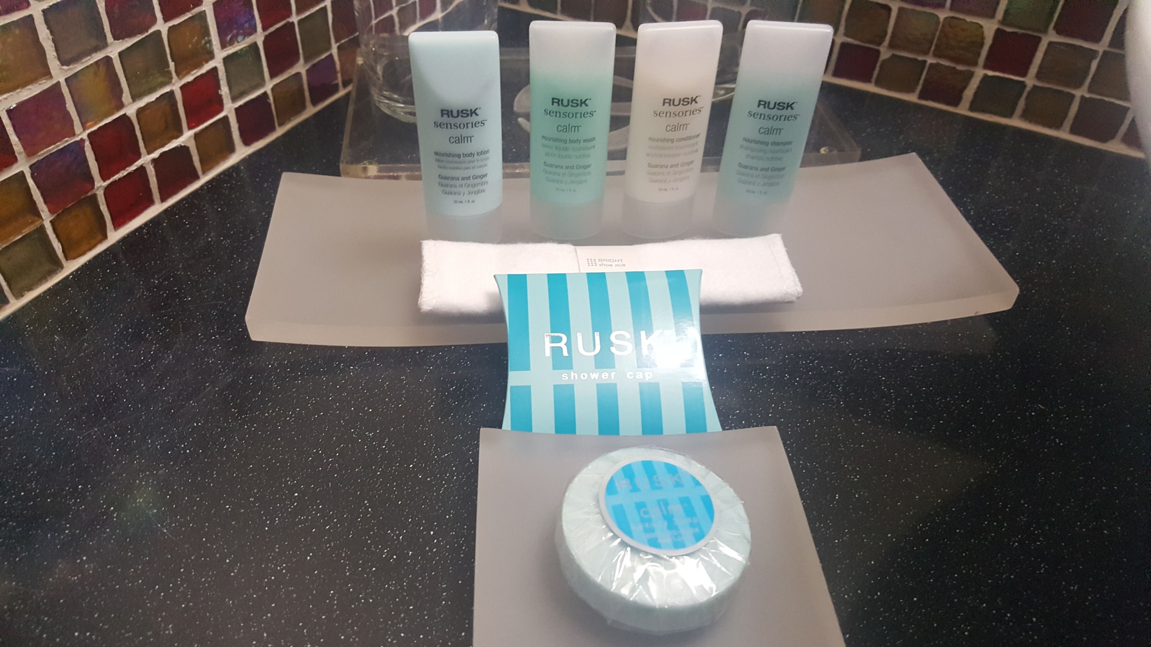 Toiletries on a countertop, including a RUSK shower cap, a RUSK body lotion, and a RUSK body wash.