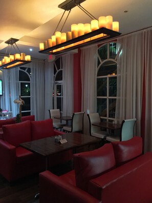 A dining area with red upholstered seating, a long table, and a chandelier with multiple light fixtures.
