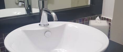 A white sink with a modern faucet, a black countertop, and a mirror above it.