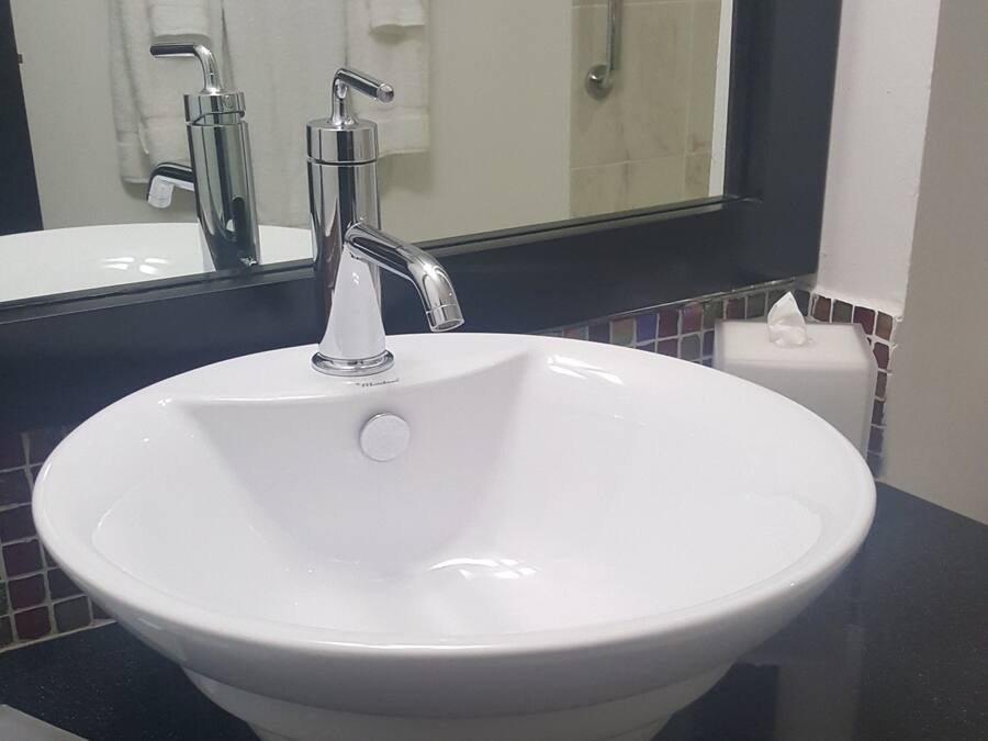 Ein weißes Waschbecken mit einem modernen Wasserhahn, einer schwarzen Arbeitsplatte und einem Spiegel darüber.