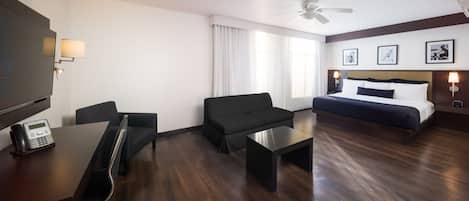 Habitación de hotel con cama, escritorio, silla, sofá, ventilador de techo y ventana con cortinas.
