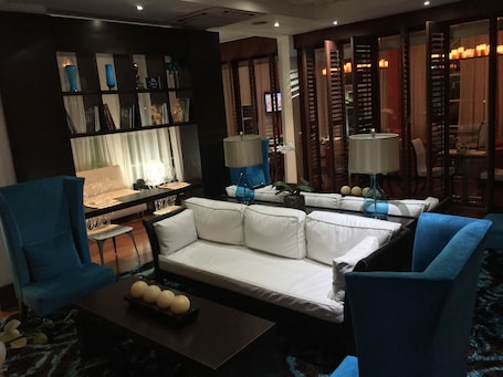 A modern living room with a white sofa, blue armchairs, a coffee table with decorative items, and a bookshelf with various objects.