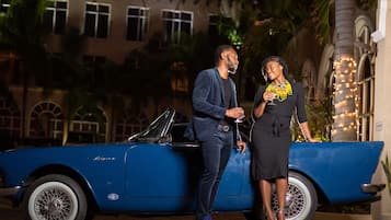A blue convertible car parked in front of a building with arched windows and a palm tree.