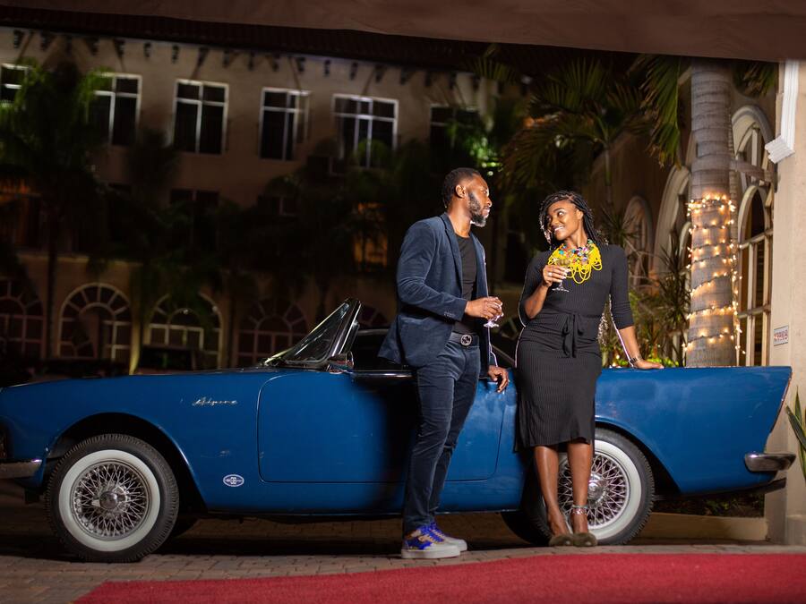 A blue convertible car parked in front of a building with arched windows and a palm tree.