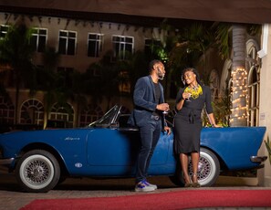 A blue convertible car parked in front of a building with arched windows and a palm tree.
