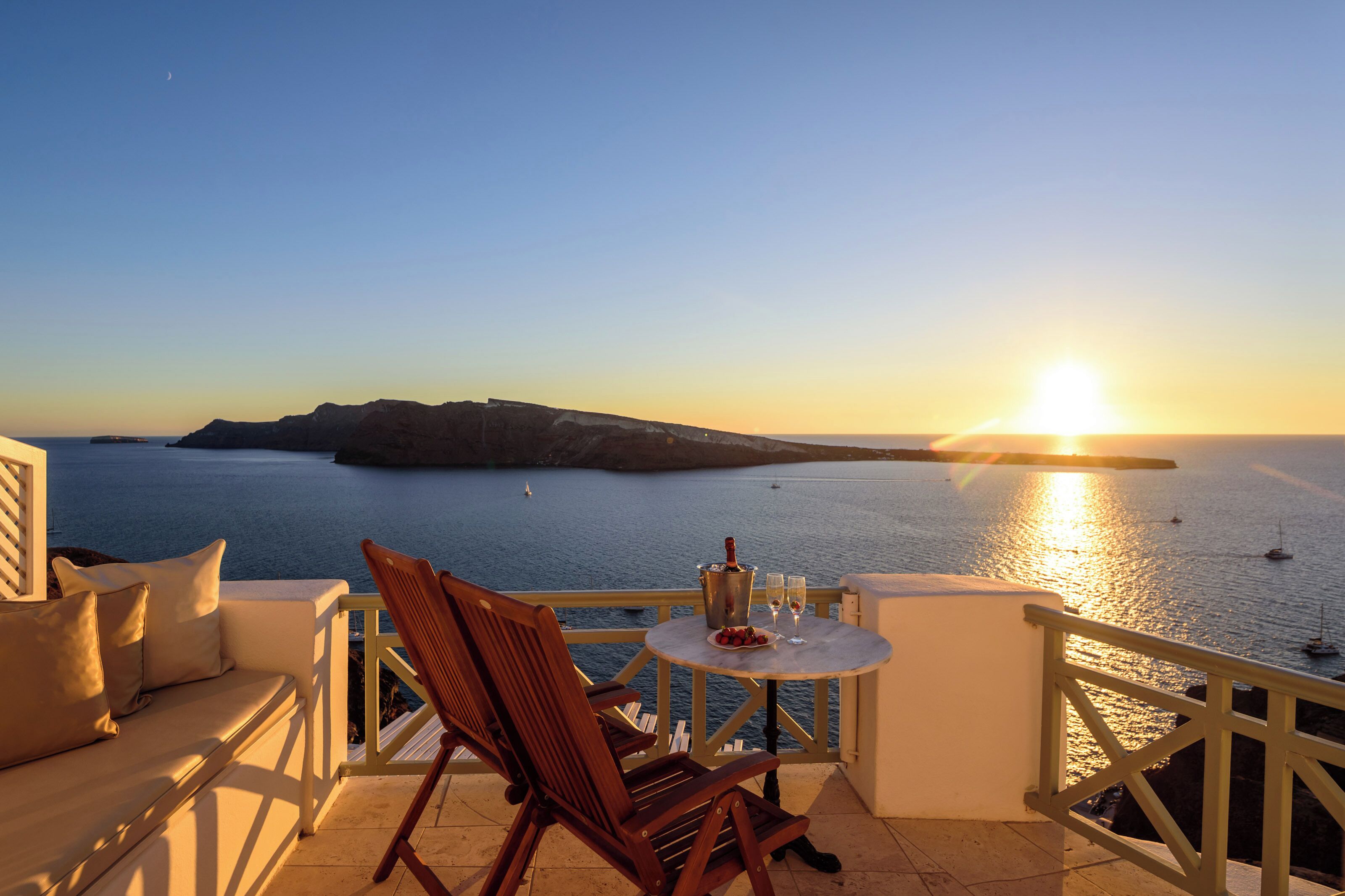 A terrace with a table, chairs, and a view of the sea at sunset.