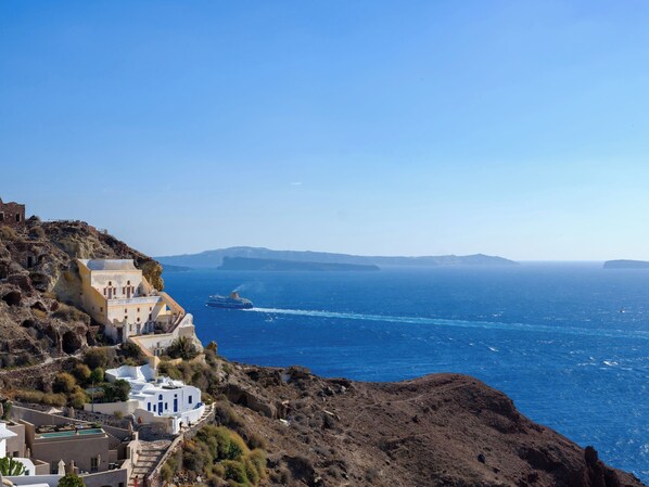 Un pueblo costero con edificios blancos, un mar azul cristalino y un crucero en la distancia.