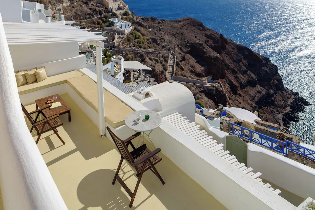 Um terraço com vista para o mar, edifícios brancos e terreno rochoso.