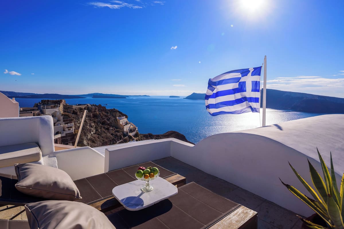 Uma varanda com uma mesa, uma bandeira e vista para o mar e ilhas ao longe.