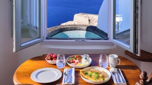 A table with breakfast items and a view of the sea through a window. - Fanari Villas Santorini (Santorini)