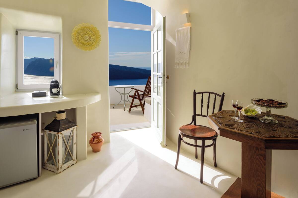 Quarto com vista para o mar, mesa de jantar com cadeiras, máquina de café e um pequeno frigorífico.
