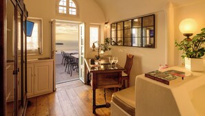 A room with a wooden floor, a dining table with chairs, a bookshelf, and a view through an open door. - Fanari Villas Santorini (Santorini)