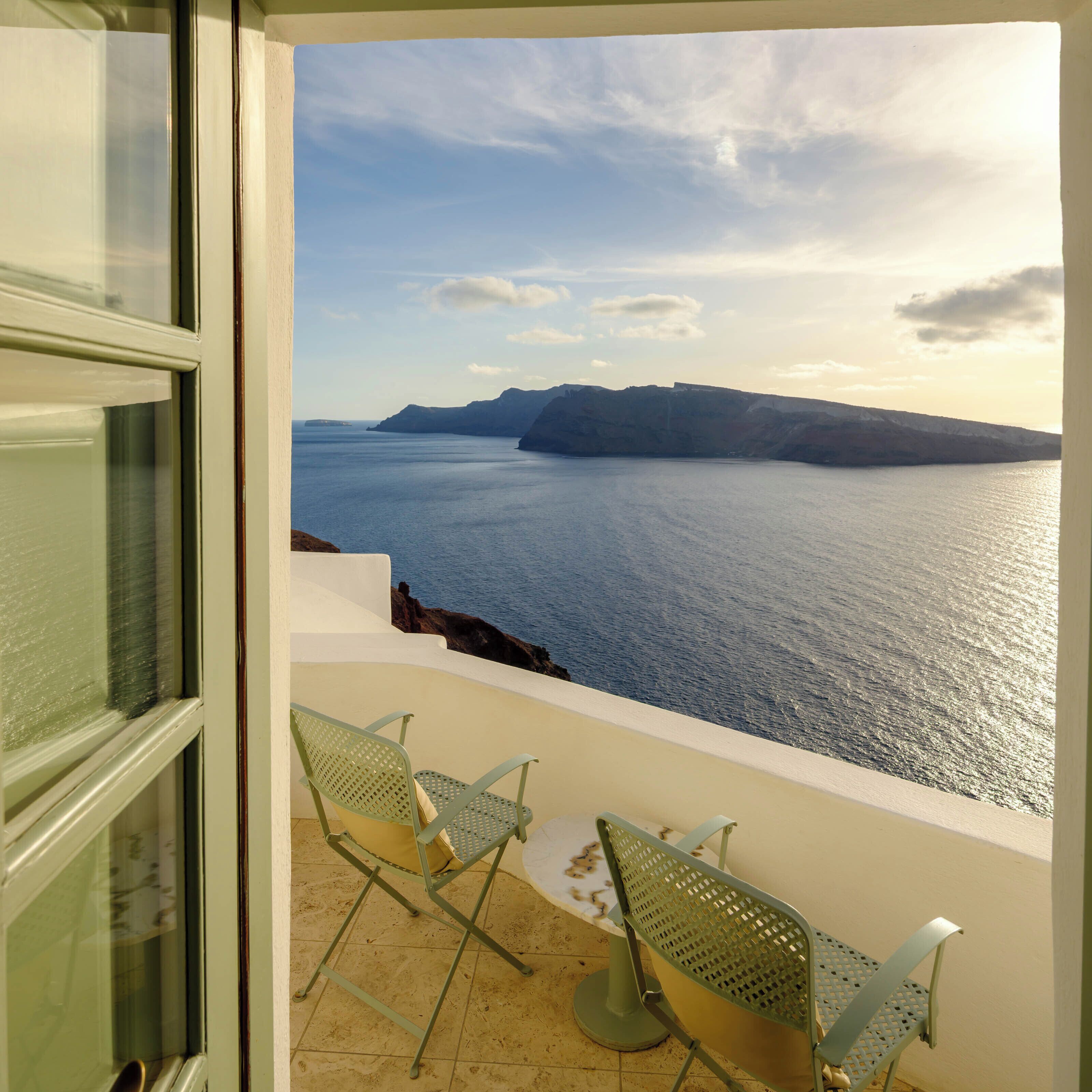 Een balkon met uitzicht op zee en kliffen. Twee metalen stoelen en een tafel staan er.