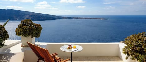 A terrace with a view of the sea, a table with a plate of food and a glass of orange juice, and two wooden chairs.