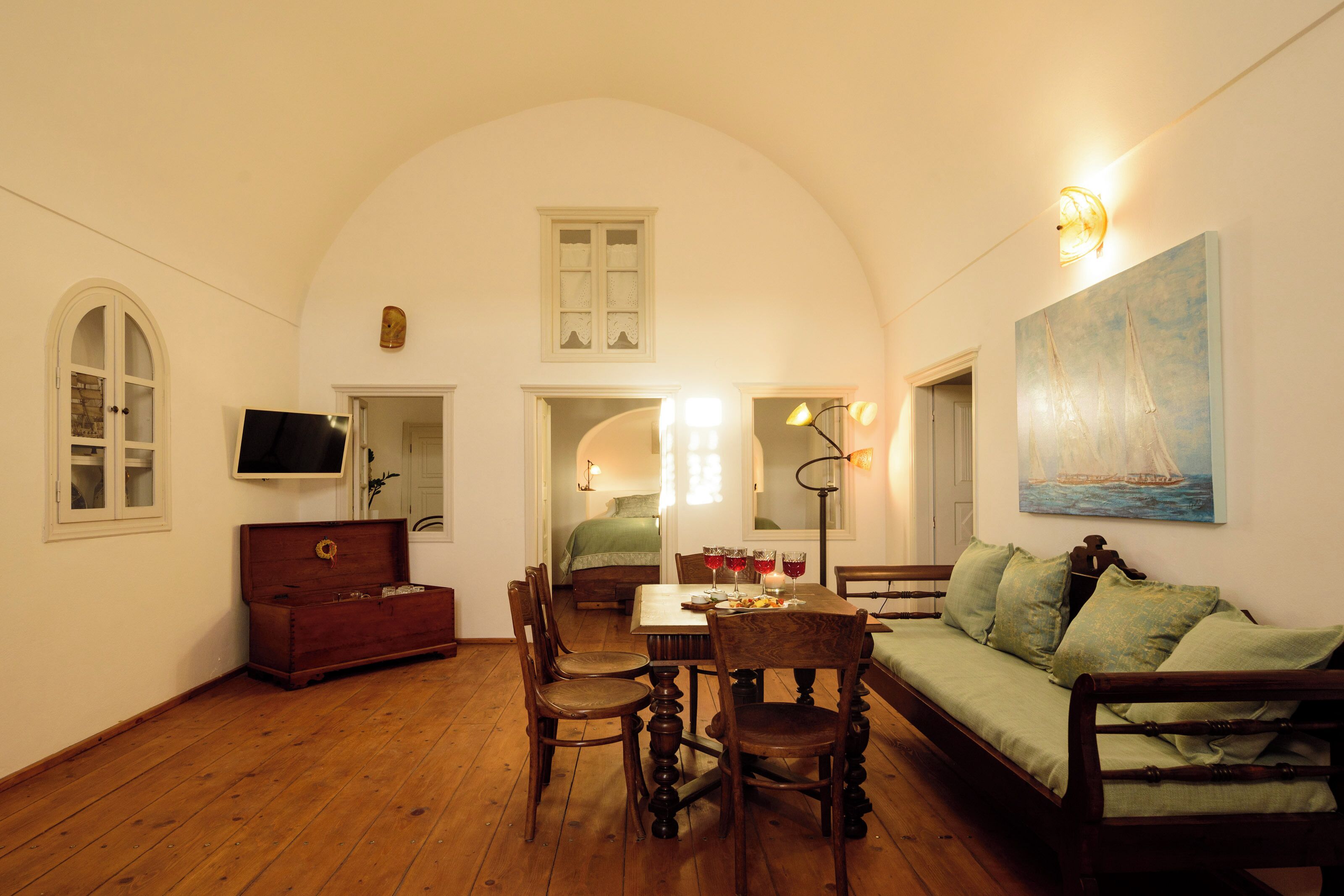 A cozy room with a wooden floor, a dining table with chairs, a sofa, a wooden chest, and a painting of sailboats.