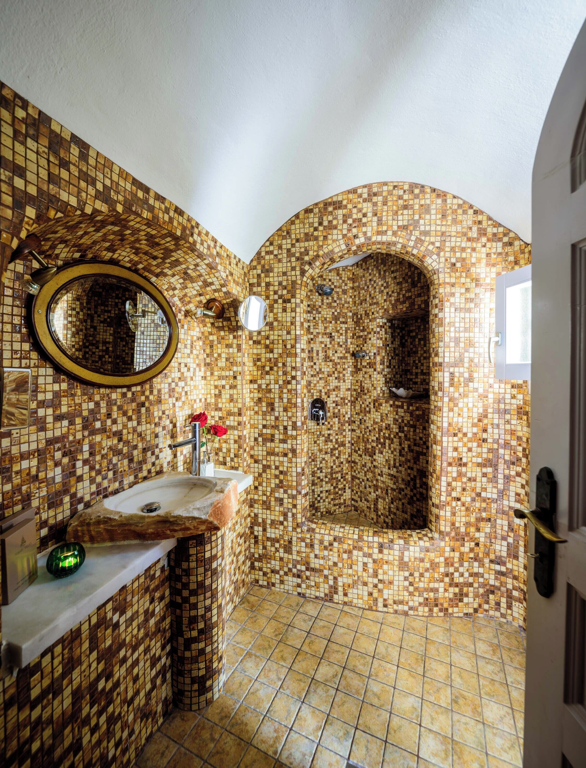 A bathroom with mosaic tile walls, a round mirror, a sink, and a shower area.