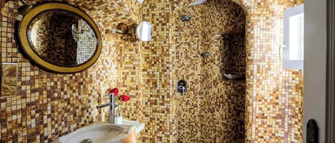 A bathroom with mosaic tile walls, a round mirror, a sink, and a shower area.