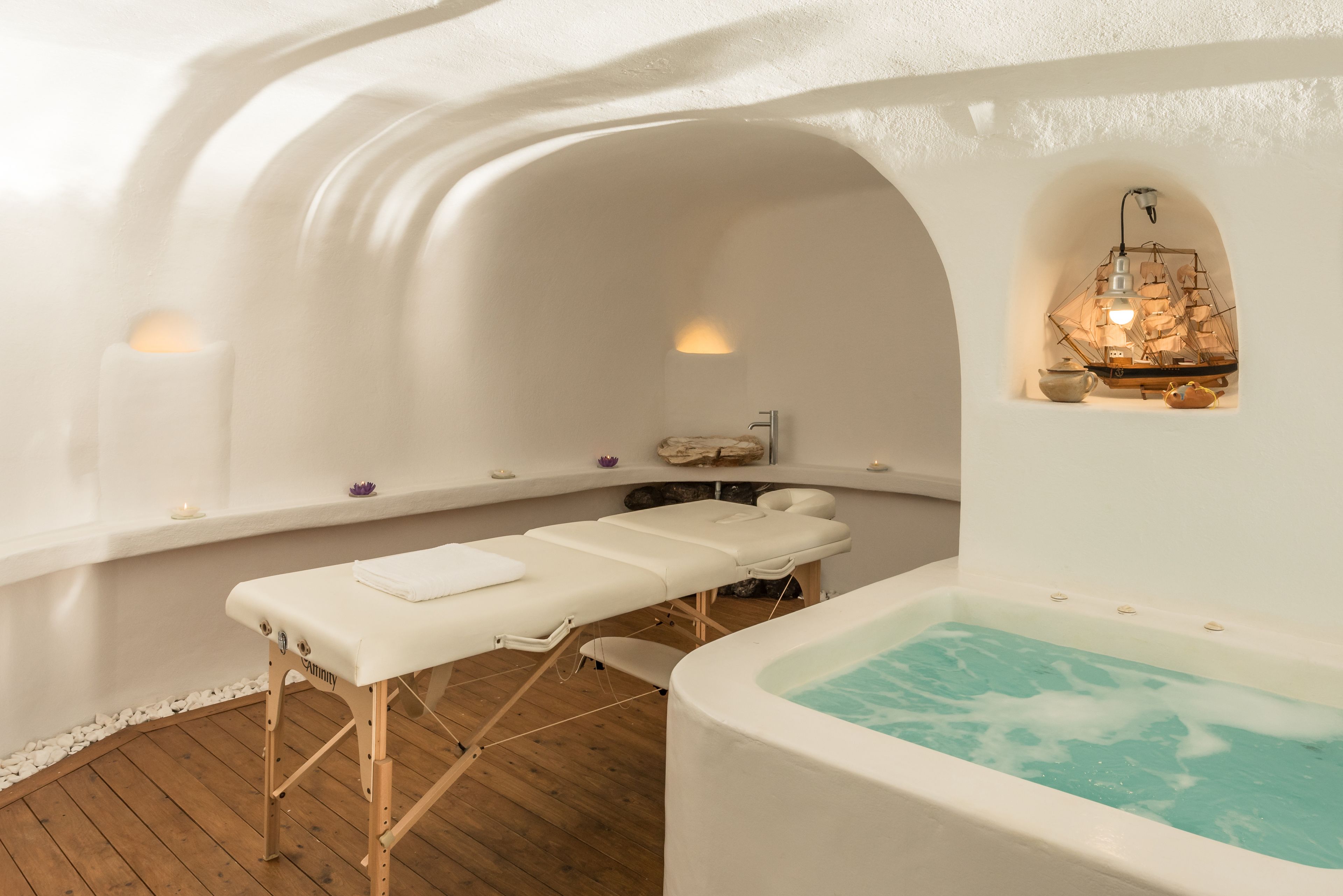 A spa room with a massage table, a hot tub, and a shelf with candles and decorative items.