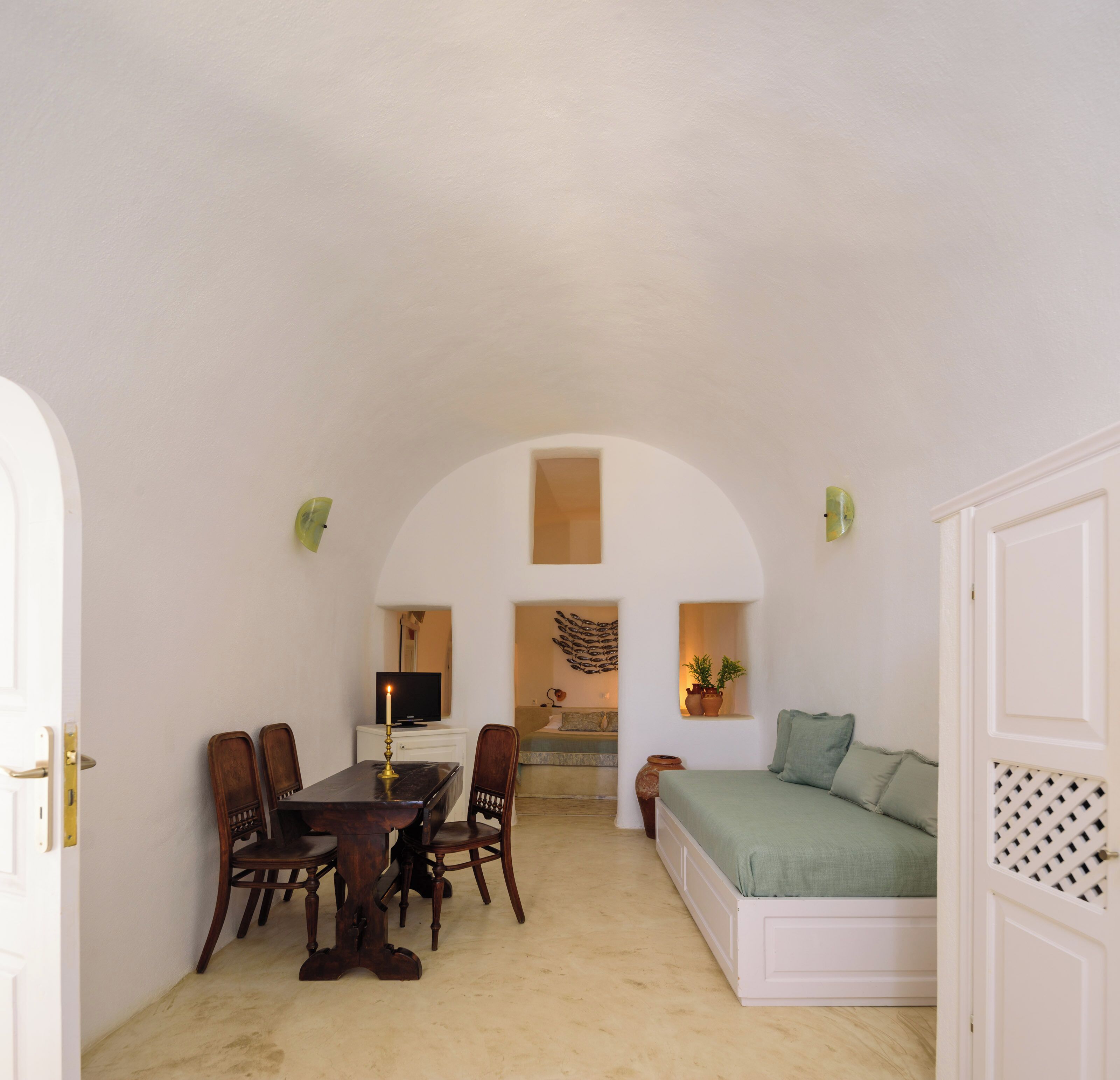 A room with a dining table, chairs, a television, a sofa, and a decorative wall piece.