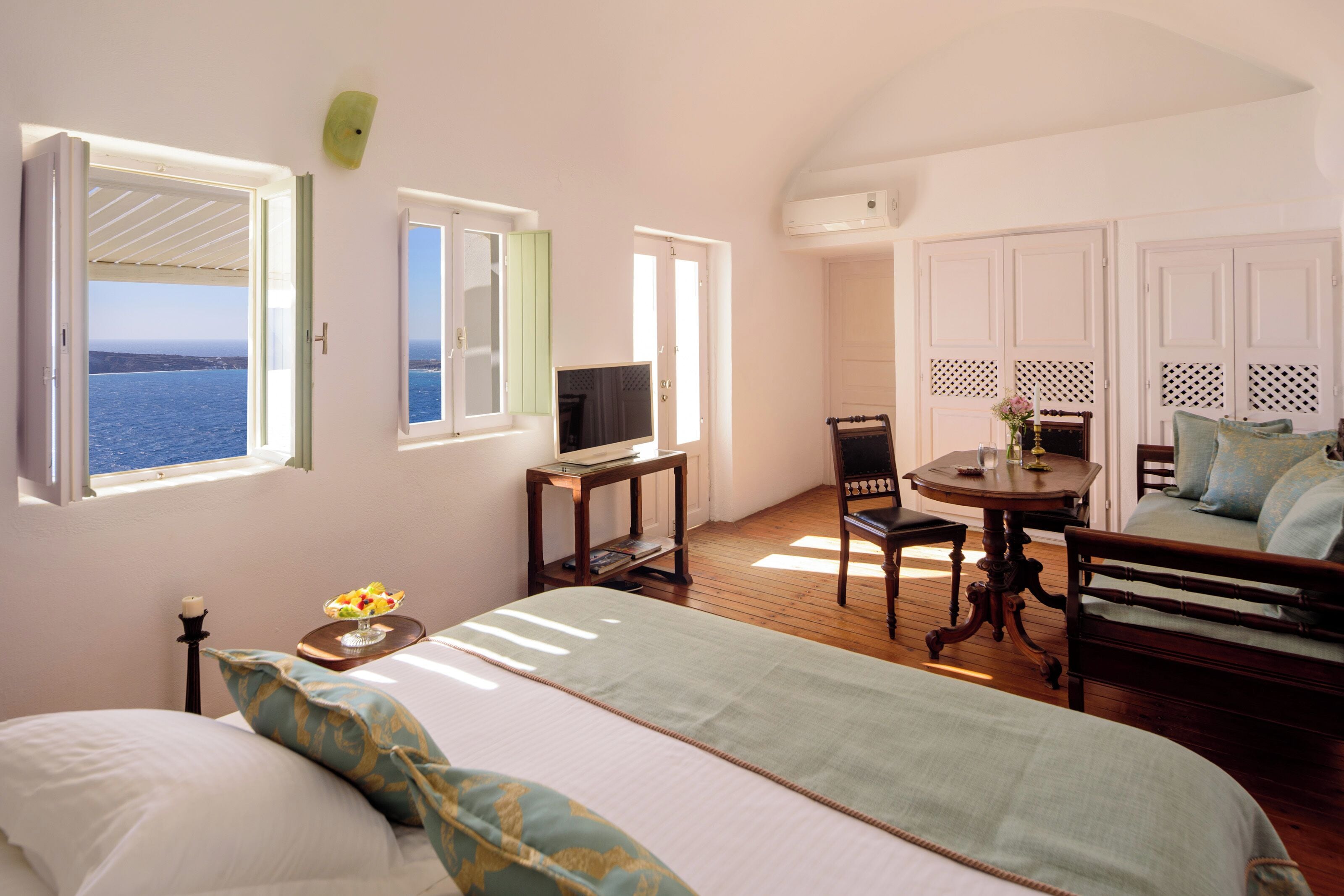 A bedroom with a bed, a desk, a chair, and a view of the sea.