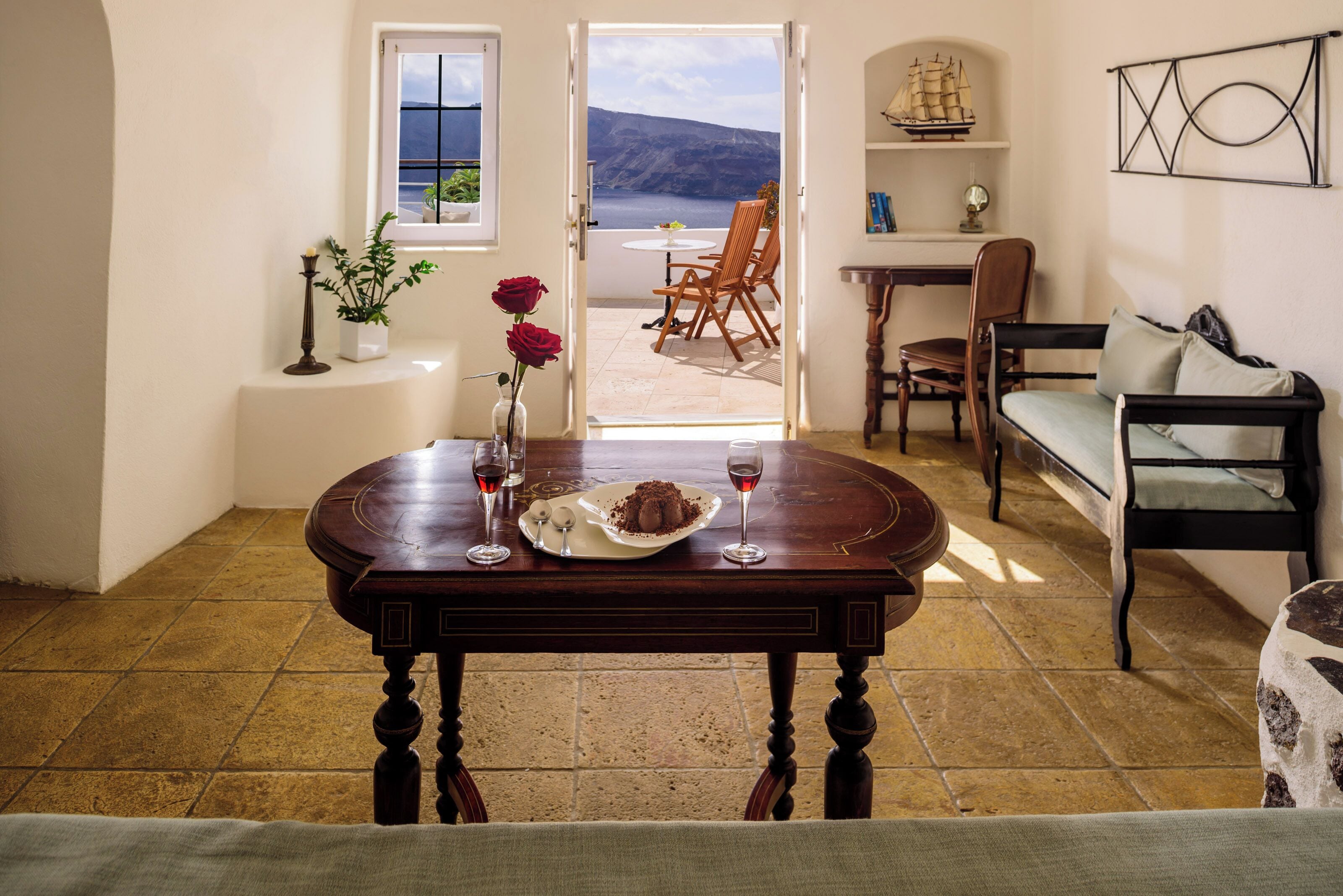 A dining area with a table set for two, a view of the sea, and a cozy seating arrangement.
