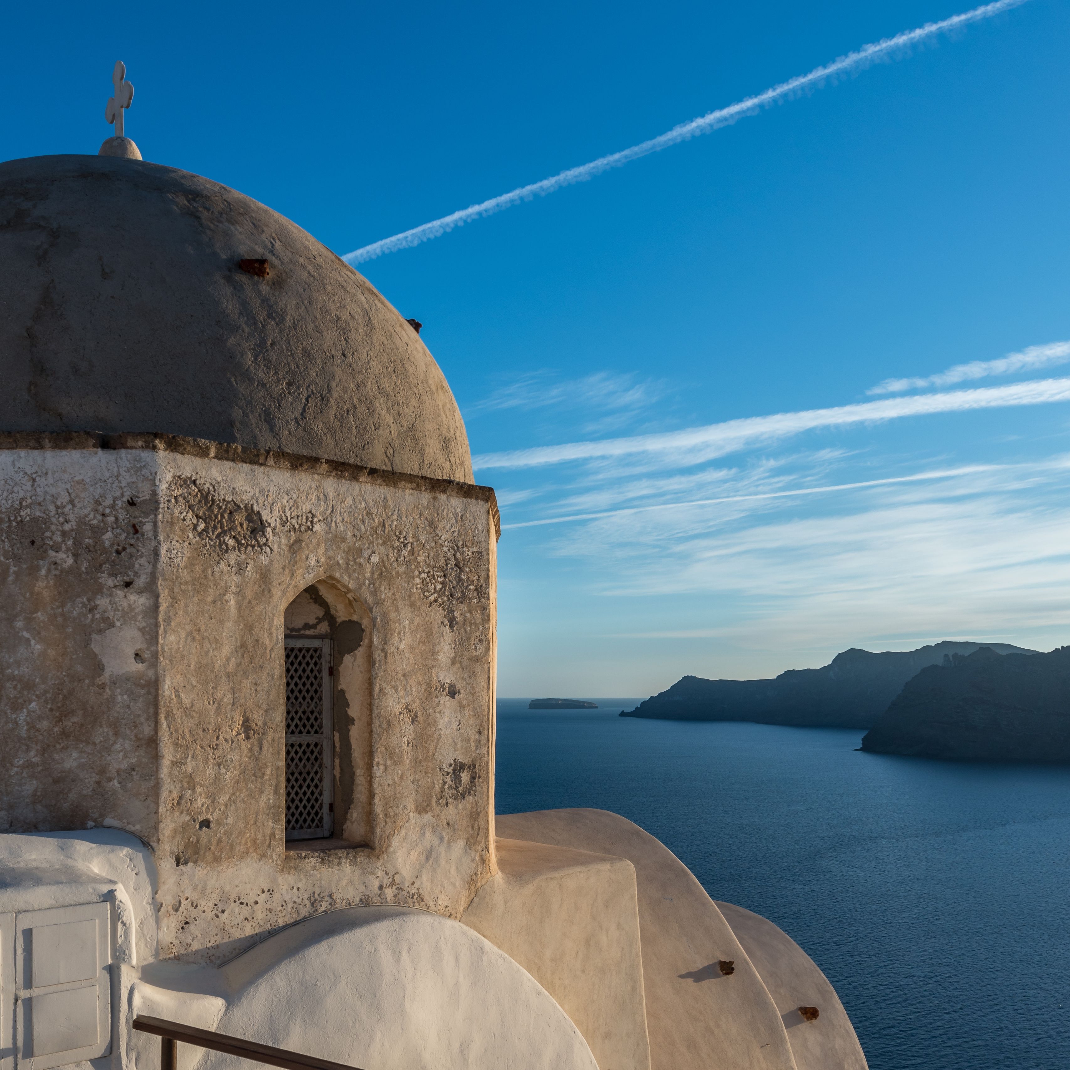A coastal building with a dome and arched window, overlooking a body of water and distant land.